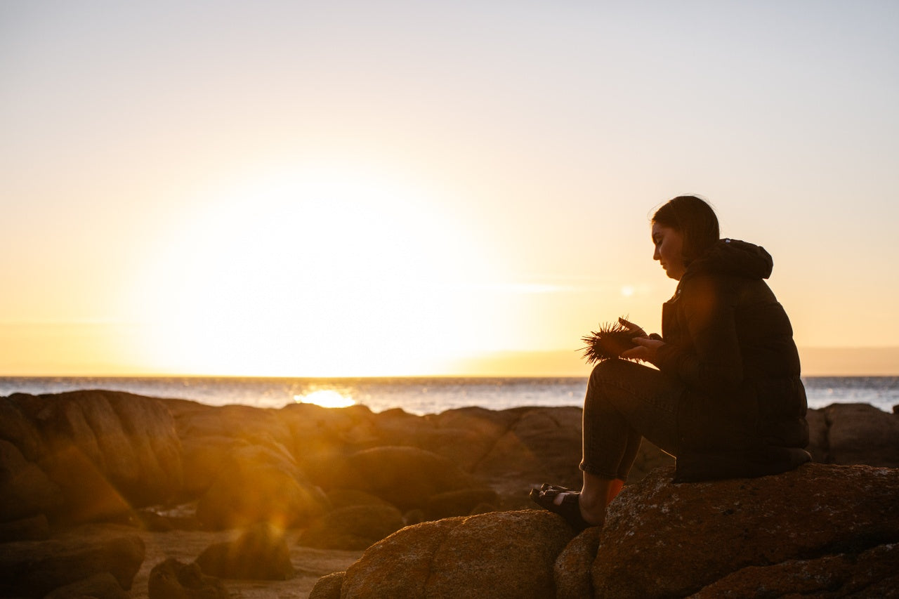 Person sitting on rocks by the ocean at sunset